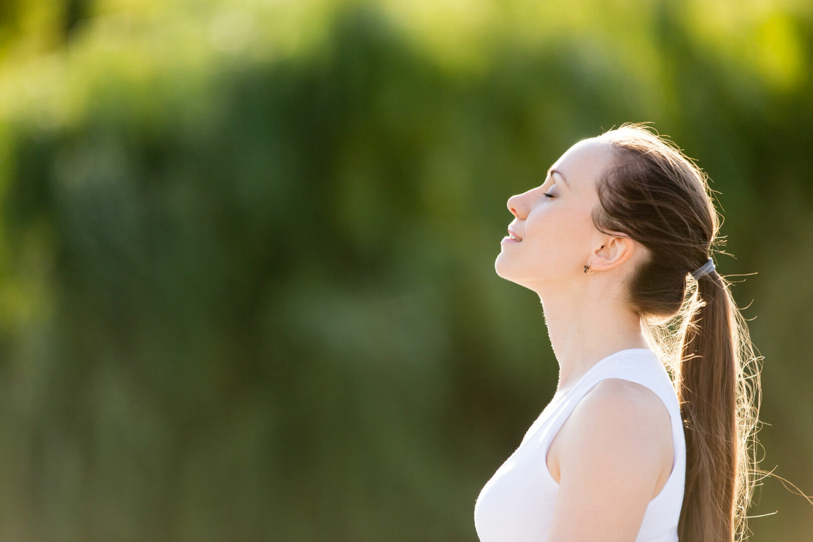 A woman is standing outside with her eyes closed.