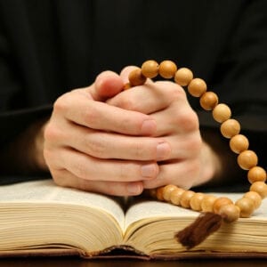 A person with their hands folded on top of an open book.