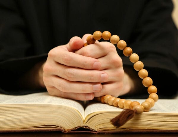 A person with their hands folded on top of an open book.