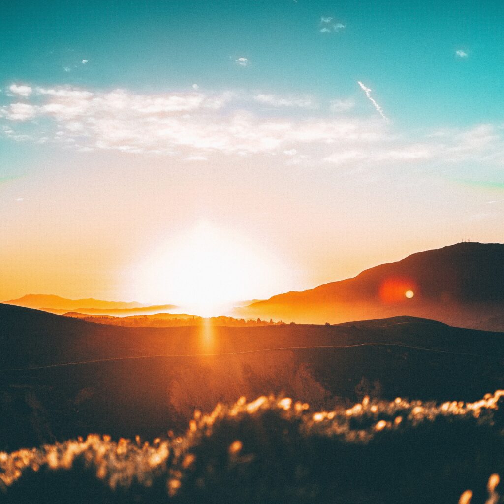 A sunset over the mountains with a sun setting.